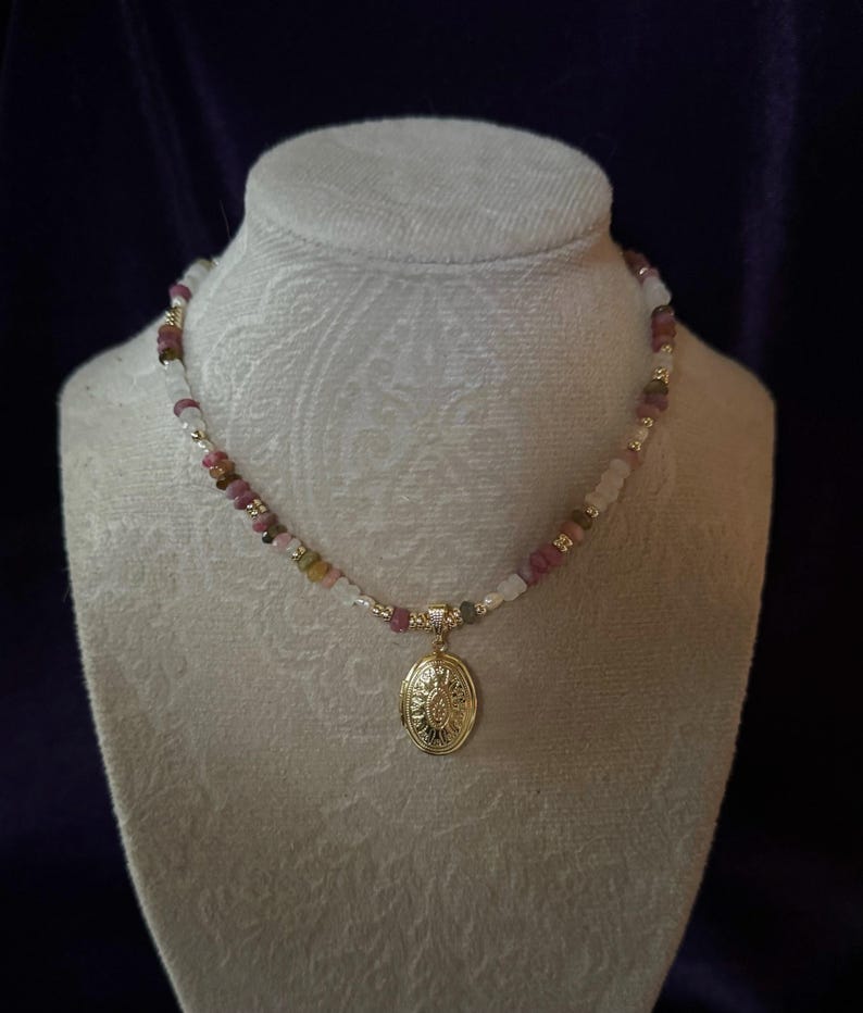 Puede incluir: Un collar de oro con un medall&oacute;n con un dise&ntilde;o floral. El collar est&aacute; hecho con cuentas rosas, blancas y marrones.