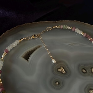 Puede incluir: Un delicado collar de cadena dorada con una variedad de cuentas de piedras preciosas de color pastel, incluyendo rosa, verde y blanco. El collar tiene un cierre de mosquet&oacute;n.