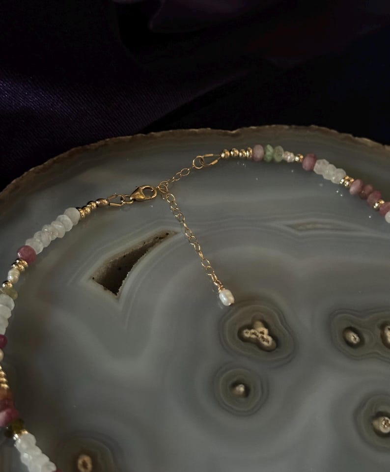 Puede incluir: Un delicado collar de cadena dorada con una variedad de cuentas de piedras preciosas de color pastel, incluyendo rosa, verde y blanco. El collar tiene un cierre de mosquet&oacute;n.