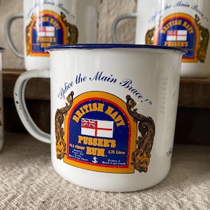 May include: White enamel mug with a blue rim and handle. The mug features a colorful emblem with the text "British Navy Pusser's Rum" and a Union Jack flag. The mug also has the text "Splice the Main Brace!"