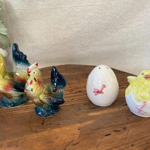 May include: A set of three ceramic mugs with a speckled, matte finish. Each mug features a different color: light blue, cream, and gray. The mugs have a simple, modern design with a rounded shape and a comfortable handle.