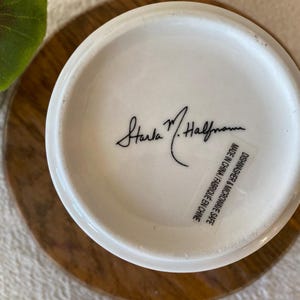 Puede incluir: Base de una taza de cer&aacute;mica blanca con la firma "Starla M. Halfmann" en escritura negra. Una etiqueta dice "Apto para lavavajillas y microondas Made in China / Fabriqu&eacute; en Chine."
