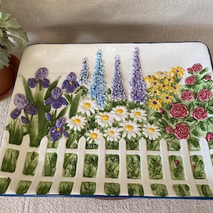 May include: Rectangular ceramic serving platter with a garden scene. Features a white picket fence with purple irises, daisies, and colorful flowers. The platter has a blue border and is a decorative piece.
