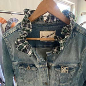 Peut inclure: Une veste en jean bleu clair avec un col &agrave; volants en tissu &agrave; carreaux vert, blanc et bleu marine. La veste pr&eacute;sente une fermeture boutonn&eacute;e, deux poches poitrine et une broche argent&eacute;e en forme d'&eacute;toile sur la poche gauche. L'&eacute;tiquette indique Remnants.