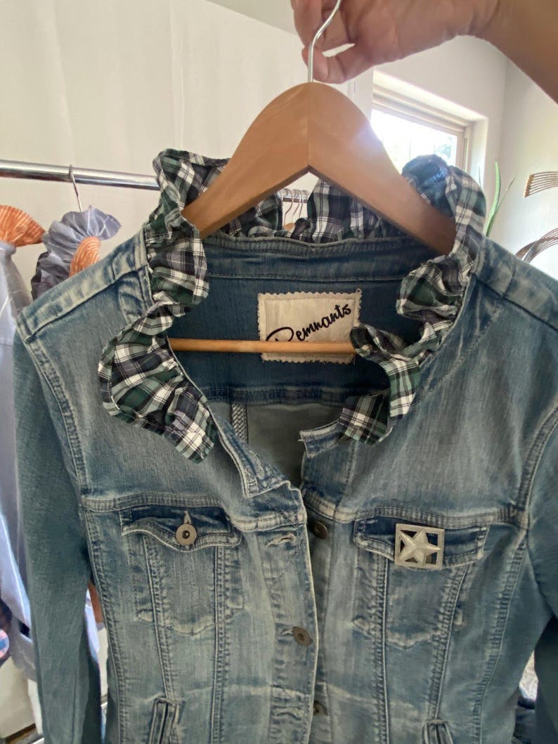 Peut inclure: Une veste en jean bleu clair avec un col &agrave; volants en tissu &agrave; carreaux vert, blanc et bleu marine. La veste pr&eacute;sente une fermeture boutonn&eacute;e, deux poches poitrine et une broche argent&eacute;e en forme d'&eacute;toile sur la poche gauche. L'&eacute;tiquette indique Remnants.