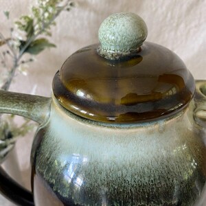 May include: A ceramic teapot with a lid and handle. The teapot has a glossy finish with a color gradient of brown, green, and light blue. The lid has a small, round knob. The spout is visible on the right side.