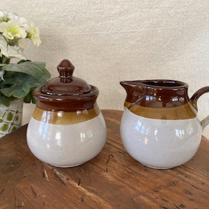 May include: A set of three ceramic mugs with a speckled, matte finish. The mugs are in shades of cream, light gray, and dark gray. Each mug has a simple, modern design and a rounded handle.
