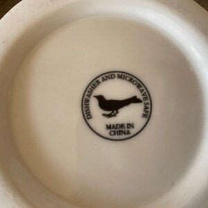 May include: A white ceramic mug base with a black circular emblem. The emblem features a bird silhouette and the text "Dishwasher and Microwave Safe" and "Made in China".