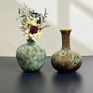 May include: Two ceramic vases with a mottled glaze. One is green and holds dried flowers. The other is brown with green accents. The vases are decorative and suitable for displaying flowers or as standalone art pieces.
