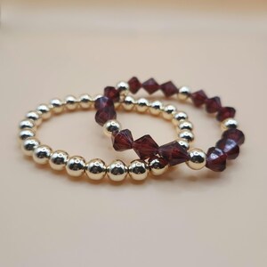 May include: Two bracelets, one with gold beads and one with dark red faceted beads.