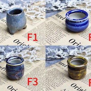 May include: Four small ceramic pots in shades of blue and yellow are displayed on a newspaper background. The pots vary in shape and texture, with one having a speckled finish and another a glossy glaze. Each pot is a miniature planter.
