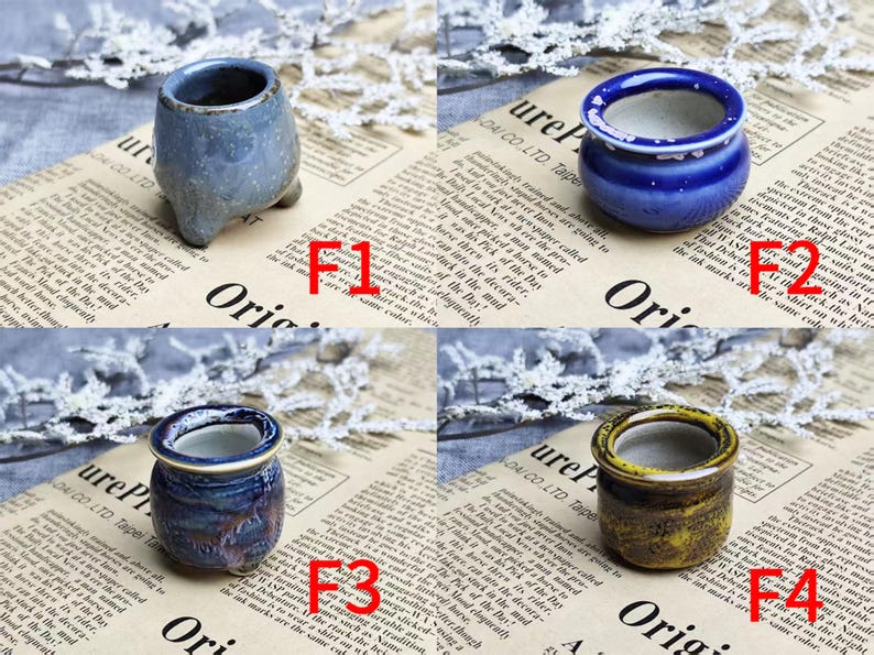 May include: Four small ceramic pots in shades of blue and yellow are displayed on a newspaper background. The pots vary in shape and texture, with one having a speckled finish and another a glossy glaze. Each pot is a miniature planter.