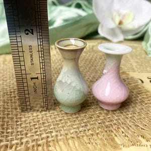 May include: Two miniature ceramic vases with a crackle glaze finish, one in pale green and one in soft pink, standing next to a stainless steel ruler that shows a height of approximately 1.5 inches for the vases.