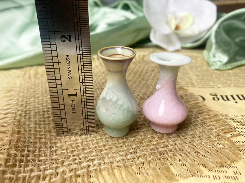 May include: Two miniature ceramic vases with a crackle glaze finish, one in pale green and one in soft pink, standing next to a stainless steel ruler that shows a height of approximately 1.5 inches for the vases.