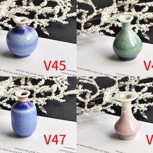 May include: Four small ceramic vases labeled V45, V46, V47, and V48. V45 is a round blue crackle-glaze vase. V46 is a teardrop-shaped green vase. V47 is a cylindrical blue crackle-glaze vase. V48 is a pink vase with a wide, flared rim.