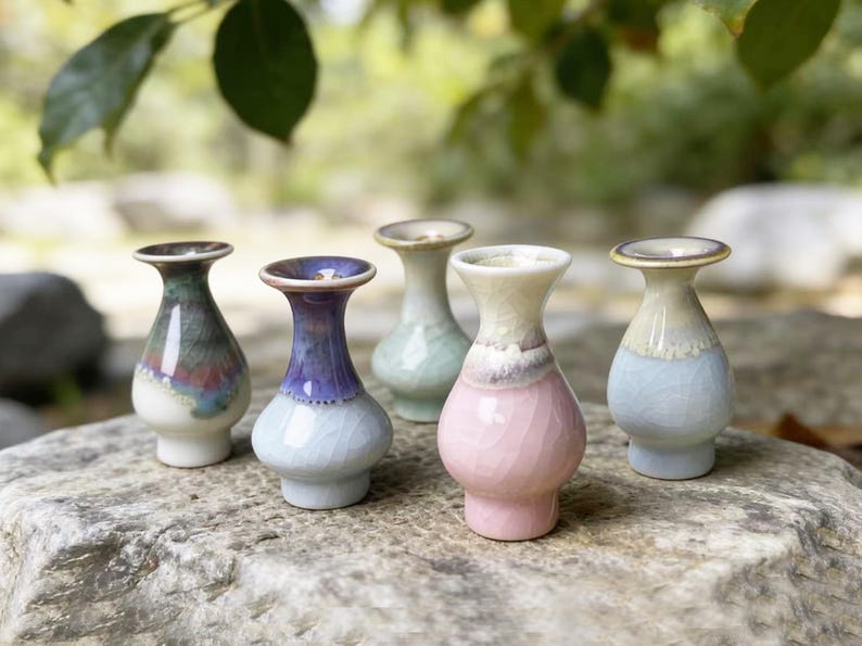 May include: Five small ceramic vases with a crackle glaze finish, each featuring a distinct color palette including pink, purple, blue, green, and white, with a bulbous body, a narrow neck, and a flared rim, arranged in a cluster.