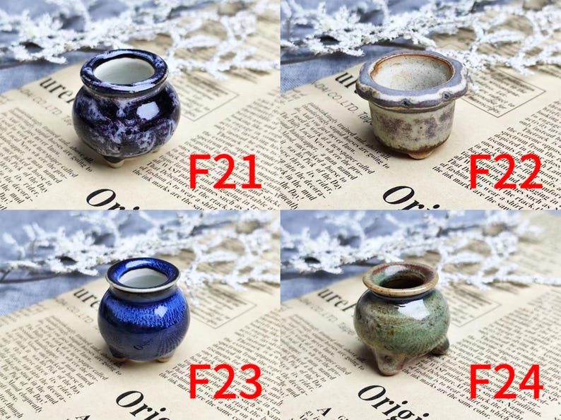 May include: Four small ceramic pots in various colors: dark blue with white swirls, beige with purple accents, cobalt blue, and green with brown trim. Each pot has a unique shape and sits on three small feet. The pots are displayed on a newspaper background.
