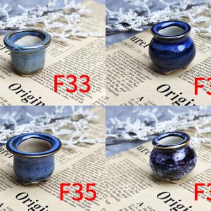 May include: Four small ceramic pots in shades of blue, each with a contrasting rim. The pots are displayed on a newspaper background with the word "Origin" visible. Each pot is labeled with a red number.