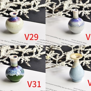 May include: Four miniature ceramic vases labeled V29, V30, V31, and V32. V29 is round with blue and cream glaze. V30 is a tall-necked blue and white vase. V31 features green, blue, and white tones. V32 is a light blue vase with a wide rim.