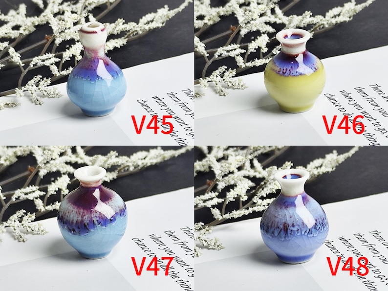 Op de afbeelding: Vier miniatuur keramische vazen gelabeld V45, V46, V47 en V48. V45 is lichtblauw met een donkerpaarse rand. V46 is geel met een donkerpaarse rand. V47 en V48 zijn lichtblauw met donkerpaarse glazuurdruppels, elk met een witte hals en rand.