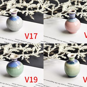 May include: Four small ceramic vases labeled V17, V18, V19, and V20. V17 is light gray, V18 is pink, V19 is light green, and V20 is a taller light green vase. Each features a flared rim and a blue-toned glaze around the neck area.