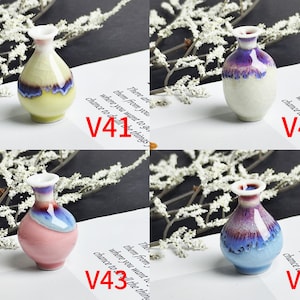 Op de afbeelding: Vier miniatuur keramische vazen gelabeld V41, V42, V43 en V44. V41 is geel met een blauwe rand, V42 is wit met een paarse rand, V43 is roze met een blauwe rand en V44 is lichtblauw met een paarse rand. Elke vaas heeft een craquel&eacute; glazuurafwerking.