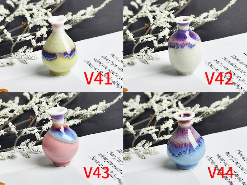 Op de afbeelding: Vier miniatuur keramische vazen gelabeld V41, V42, V43 en V44. V41 is geel met een blauwe rand, V42 is wit met een paarse rand, V43 is roze met een blauwe rand en V44 is lichtblauw met een paarse rand. Elke vaas heeft een craquel&eacute; glazuurafwerking.