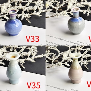 May include: Four small ceramic vases labeled V33, V34, V35, and V36. V33 is blue with a crackle glaze. V34 is gray and blue with a crackle glaze. V35 is light blue with a crackle glaze. V36 is light pink and cream with a crackle glaze.