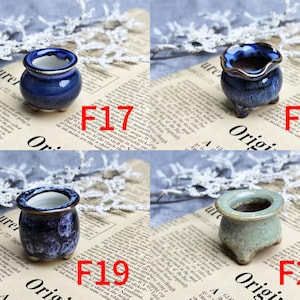 May include: Four small ceramic pots in shades of blue and green are displayed on a newspaper background. Each pot has a unique shape and finish, with variations in color and texture. The pots are labeled with the numbers F17, F18, F19, and F20.