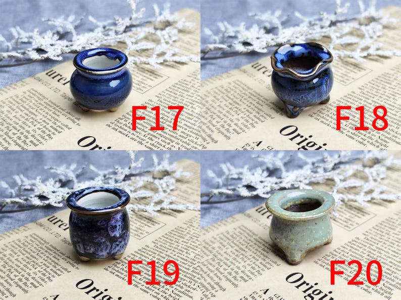 May include: Four small ceramic pots in shades of blue and green are displayed on a newspaper background. Each pot has a unique shape and finish, with variations in color and texture. The pots are labeled with the numbers F17, F18, F19, and F20.