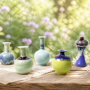 May include: Five small ceramic vases with varied shapes and glossy finishes. The collection includes a blue speckled vase, a pale green vase with a dark rim, a light blue slender vase, a bright lime green vase with a dark blue top, and a tall blue vase.