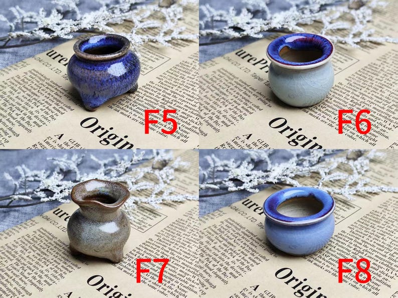May include: Four small ceramic pots in various colors: blue, gray, and brown. Each pot has a unique shape and design, with a glossy finish. The pots are displayed on a newspaper background with white floral accents.