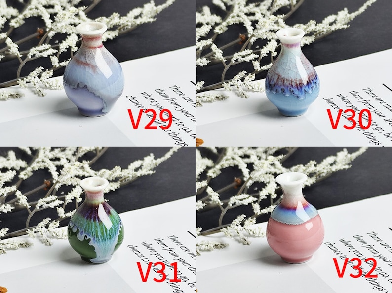 Op de afbeelding: Vier miniatuur keramische vazen met glanzende, reactieve glazuren. V29 is lichtblauw en wit, V30 is blauw en bruin, V31 is groen en paars, en V32 is roze en blauw. Elke vaas heeft een smalle hals en een ronde vorm op wit papier.
