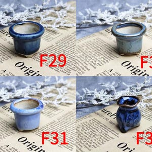 May include: Four small ceramic pots in shades of blue. The pots are labeled F29, F30, F31, and F32. The pots are on a newspaper background with white lace accents. The pots have a glossy finish.