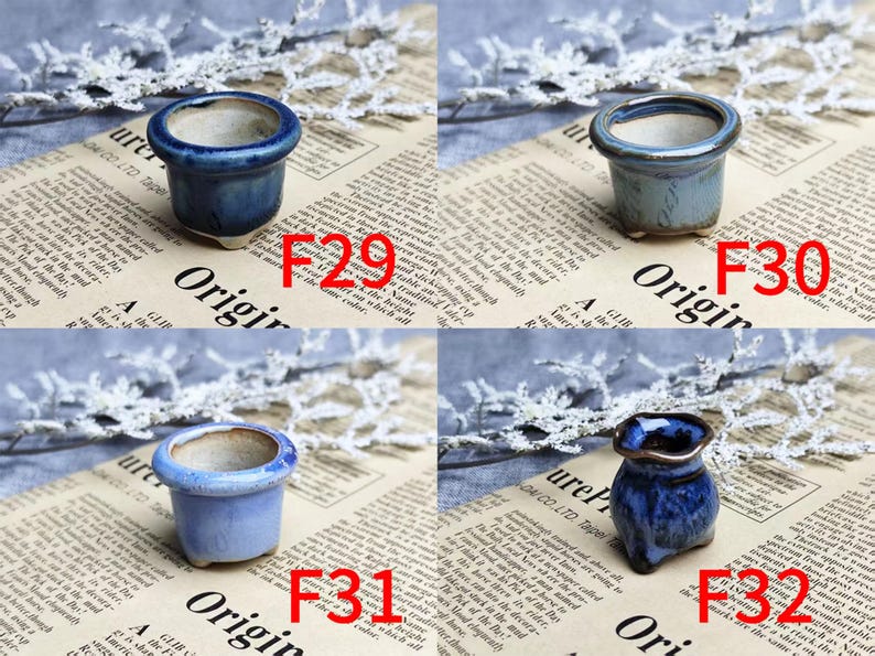 May include: Four small ceramic pots in shades of blue. The pots are labeled F29, F30, F31, and F32. The pots are on a newspaper background with white lace accents. The pots have a glossy finish.