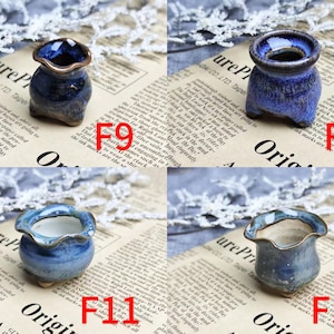 May include: Four small, handcrafted ceramic pots in shades of blue and brown. Each pot has a unique shape and glaze, with a wavy rim. The pots are displayed on a newspaper background.