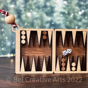 May include: A wooden backgammon board ornament with a red and white string for hanging. The board is open and shows two white dice and some checkers.
