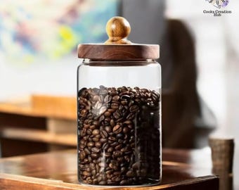 May include: A clear glass jar with a wooden lid and a wooden knob. The jar is filled with coffee beans.