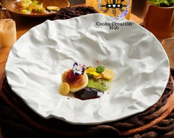 May include: A white, textured ceramic plate with a small, round, white and brown dish topped with red caviar, a yellow flower, and green sauce. The plate is on a brown woven surface.