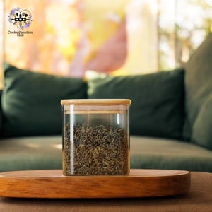 May include: A glass jar with a bamboo lid filled with loose leaf green tea. The jar is sitting on a wooden surface.
