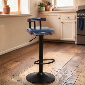 Op de afbeelding: Blauwe en zwarte verstelbare barkruk met rugleuning. De zitting is rond en heeft een gehamerde rand. De rugleuning is van hout. De kruk heeft een zwart metalen onderstel en voetsteun. De kruk staat in een keuken.