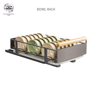 Puede incluir: Un estante para cuencos de metal negro con un asa de madera. El estante está lleno de cuencos verdes y beige. El estante está etiquetado como "BOWL RACK".