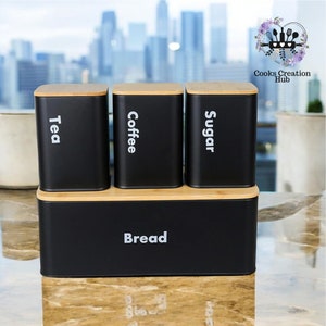 Könnte beinhalten: Ein schwarzes Küchenbehälter-Set mit Bambusdeckeln. Das Set enthält Behälter mit den Aufschriften "Tea", "Coffee", "Sugar" und "Bread". Die Behälter sind rechteckig und stehen auf einem Bambussockel.