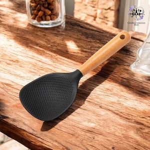 Può includere: Una paletta per riso in silicone nero con manico in legno. La paletta ha una superficie testurizzata con piccoli fori per drenare il liquido in eccesso.