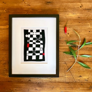 May include: A framed black and white abstract art print with red and white geometric shapes on a black and white checkered background.