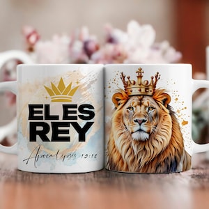 Puede incluir: Dos tazas de cerámica blanca con un diseño negro y dorado. Una taza presenta un león con una corona dorada y el texto "EL ES REY" con las palabras "Apocalipsis 13:16" debajo. La otra taza presenta una corona dorada y el texto "EL ES REY".