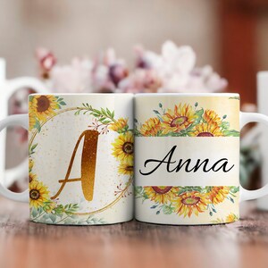 Pu&ograve; includere: Due tazze in ceramica bianca con un design a girasole. Una tazza ha la lettera "A" in glitter dorato e l'altra tazza ha il nome "Anna" in scrittura nera.