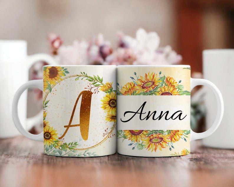 Pu&ograve; includere: Due tazze in ceramica bianca con un design a girasole. Una tazza ha la lettera "A" in glitter dorato e l'altra tazza ha il nome "Anna" in scrittura nera.