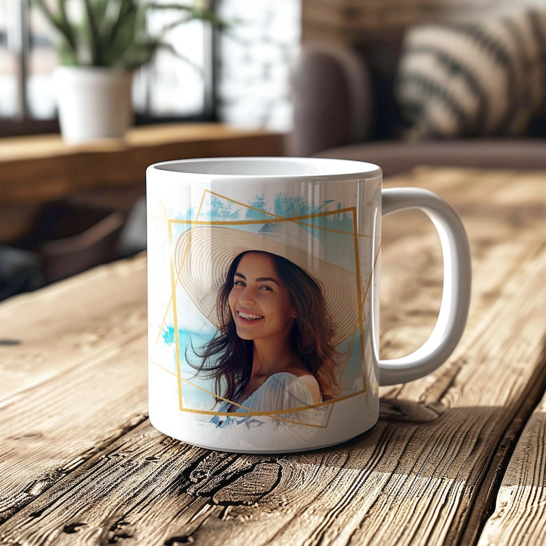 May include: White ceramic mug with a gold geometric design and a photo of a woman wearing a straw hat. The photo is set against a blue and white background.