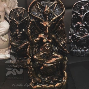May include: A gold-colored statue of a demon with wings and horns, sitting on a throne. The statue is made of resin and has a detailed design. The statue is about 6 inches tall.